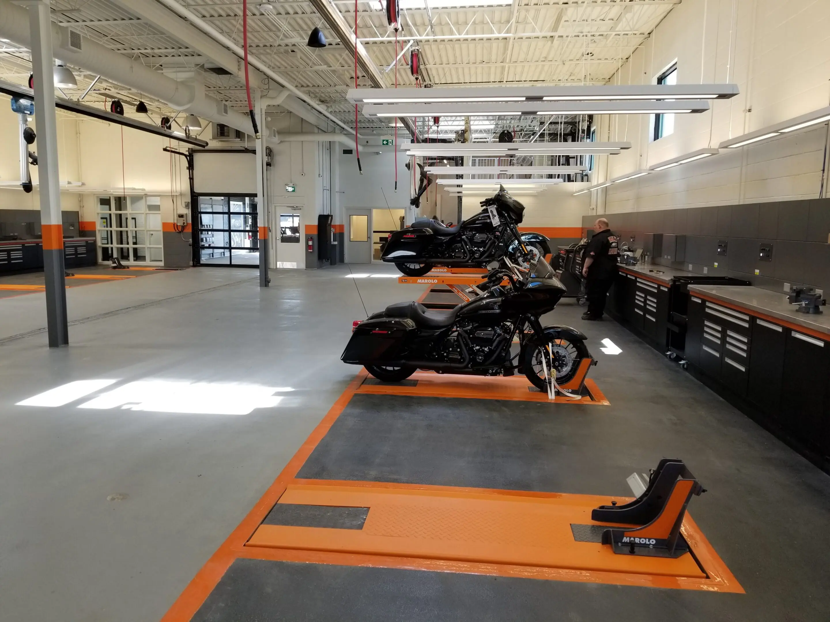 A black motorcycle parked in a spacious indoor showroom with orange markings on the floor.